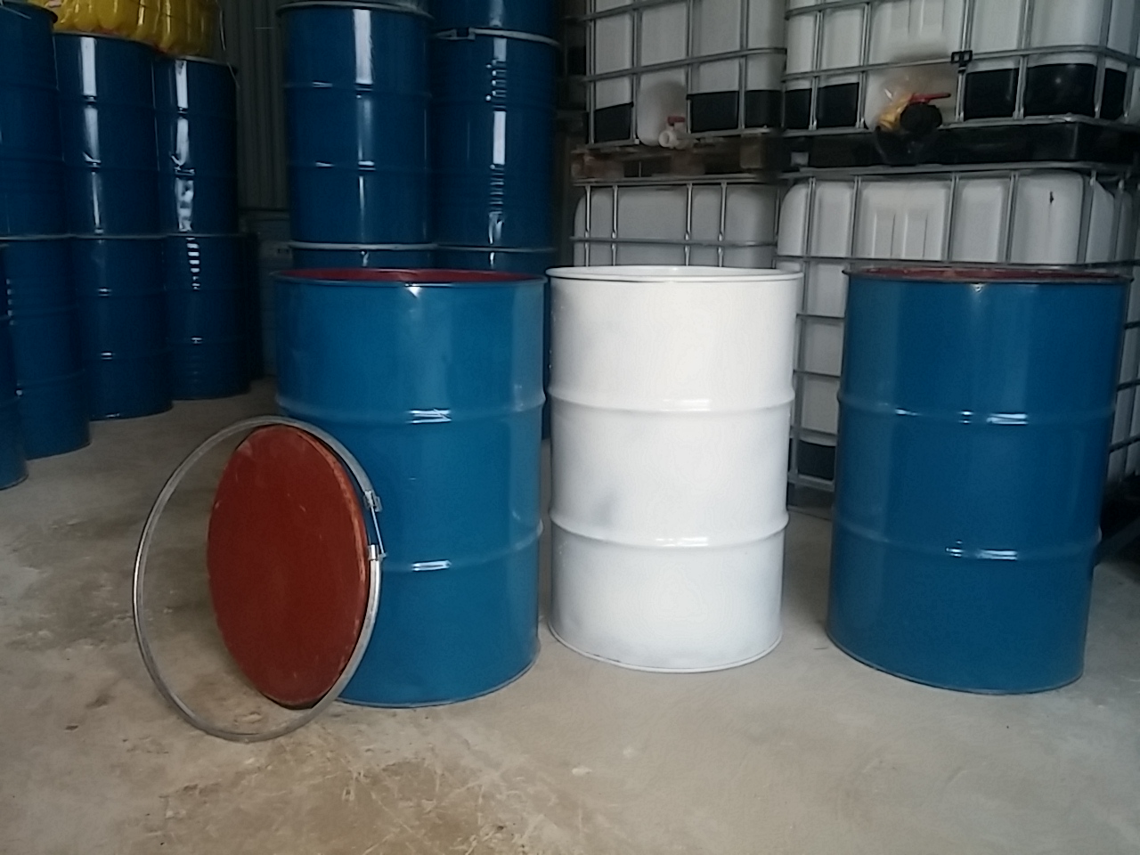 Ba thùng phuy sắt nắp mở trong kho, hai thùng sơn xanh dương và một thùng trắng, nắp tráng đỏ có vòng đai dựng bên cạnh