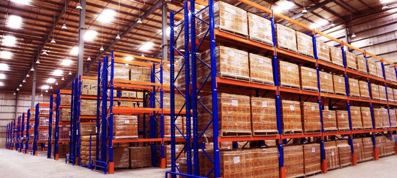 Kệ kho nhiều tầng khung xanh và cam, mỗi tầng xếp các pallet chất đầy thùng hàng
