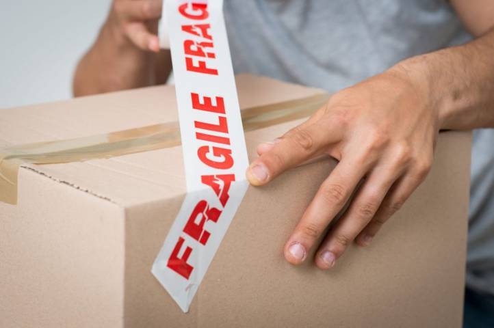 Tay dán băng dính in chữ FRAGILE đỏ trên nền trắng lên thùng carton