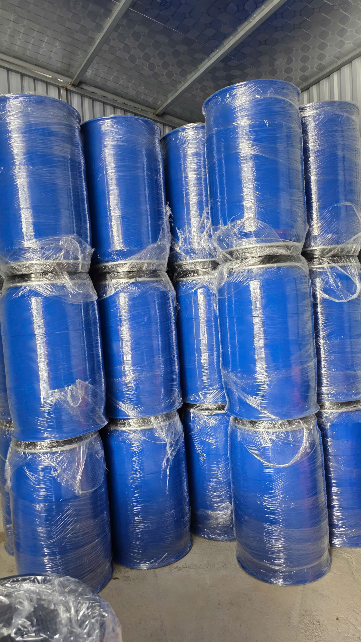 Các phuy nhựa xanh dương bọc màng co xếp chồng hai ba tầng trong kho