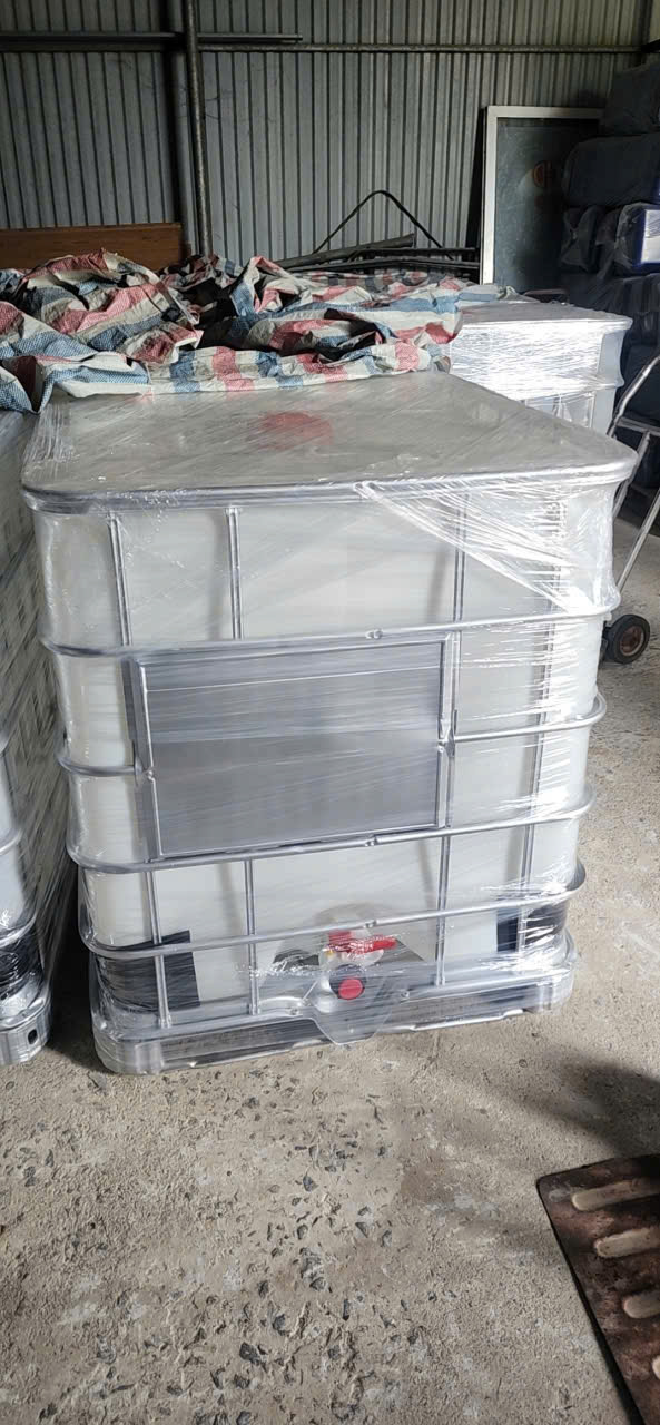 Bồn IBC trắng khung thép bọc màng co, vòi xả đỏ, đặt trong kho tôn