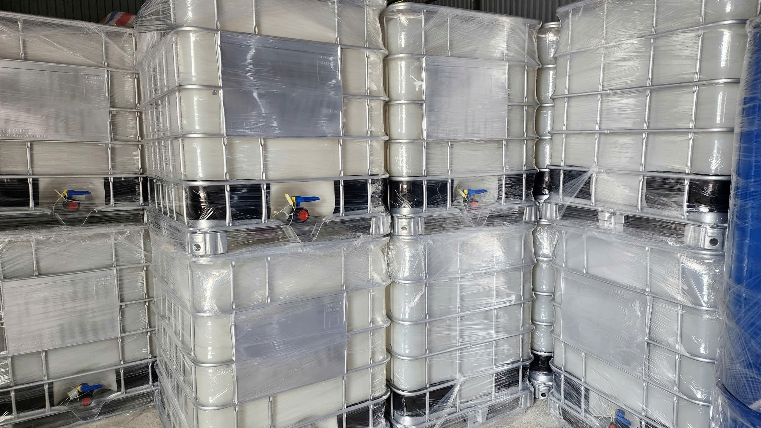 Các bồn IBC trắng đục khung thép bọc màng co xếp sát nhau trong kho