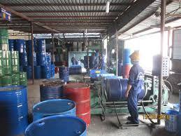 Công nhân làm việc cạnh máy trong xưởng có nhiều phuy sắt xanh đỏ