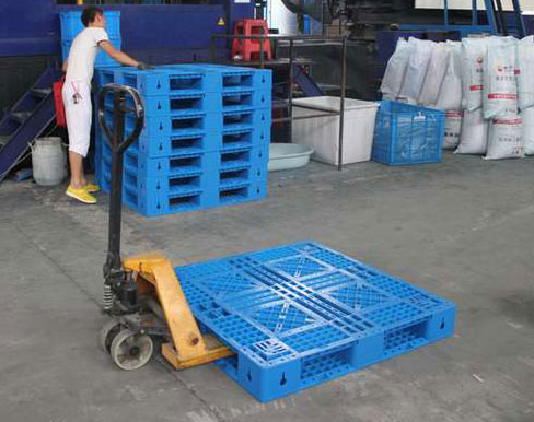 Công nhân dùng xe nâng tay kéo pallet nhựa xanh dương trong xưởng
