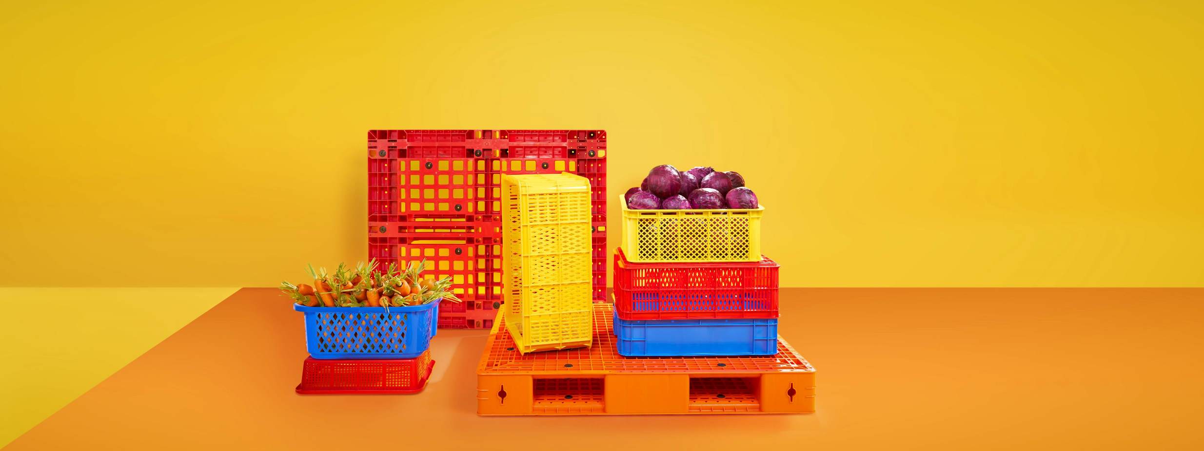 Pallet nhựa cam và đỏ cùng rổ nhựa đựng cà rốt trên nền vàng cam
