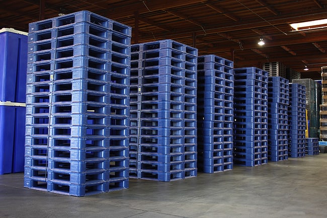Nhiều cột pallet nhựa xanh dương xếp chồng khít trong nhà kho